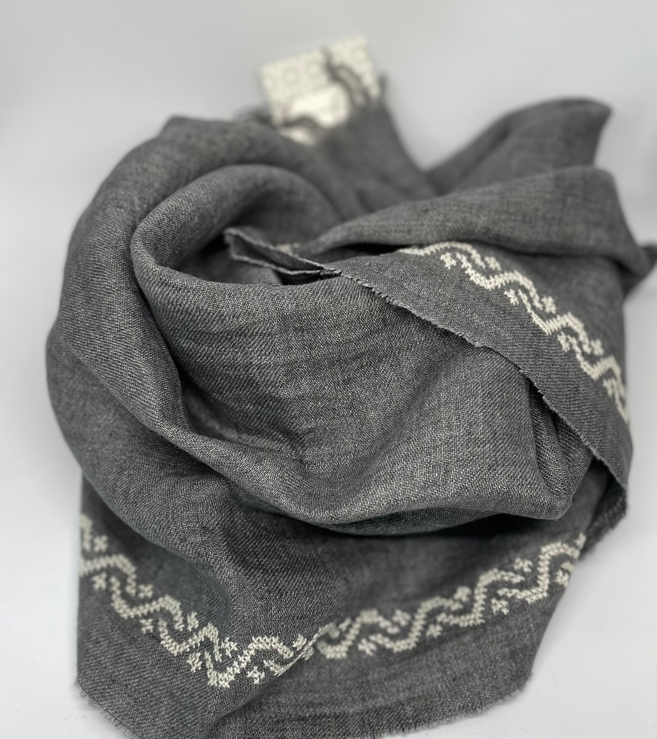 Grey linen shawl featuring ecru waves pattern, handcrafted in Italy and hand-embroidered in Jordan.