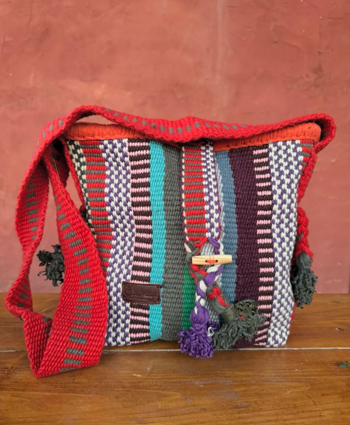 Multicolored woven bag with red trim on a wooden surface against a red background