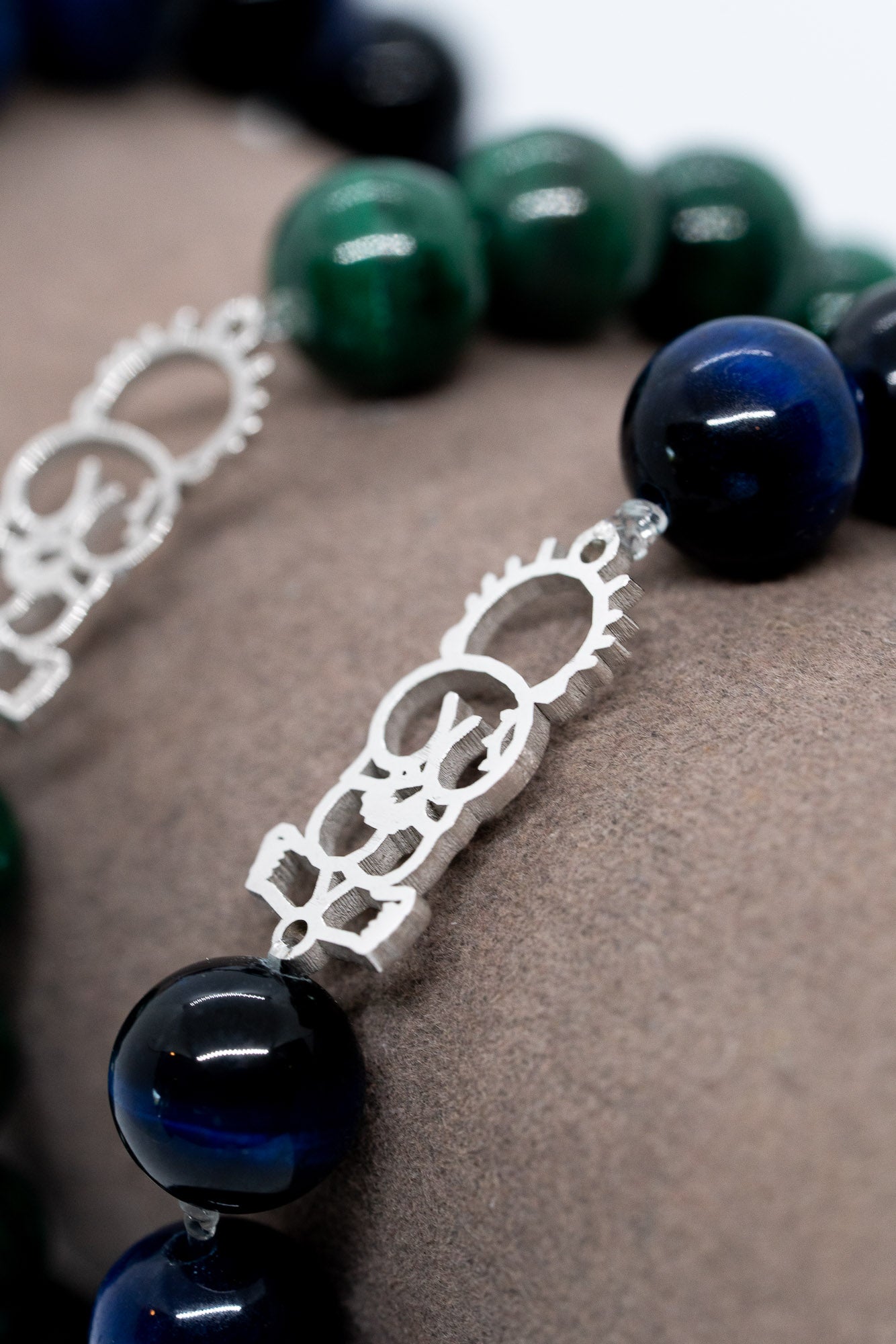Close-up of a bracelet with blue and green beads and intricate silver clasp on a textured surface.