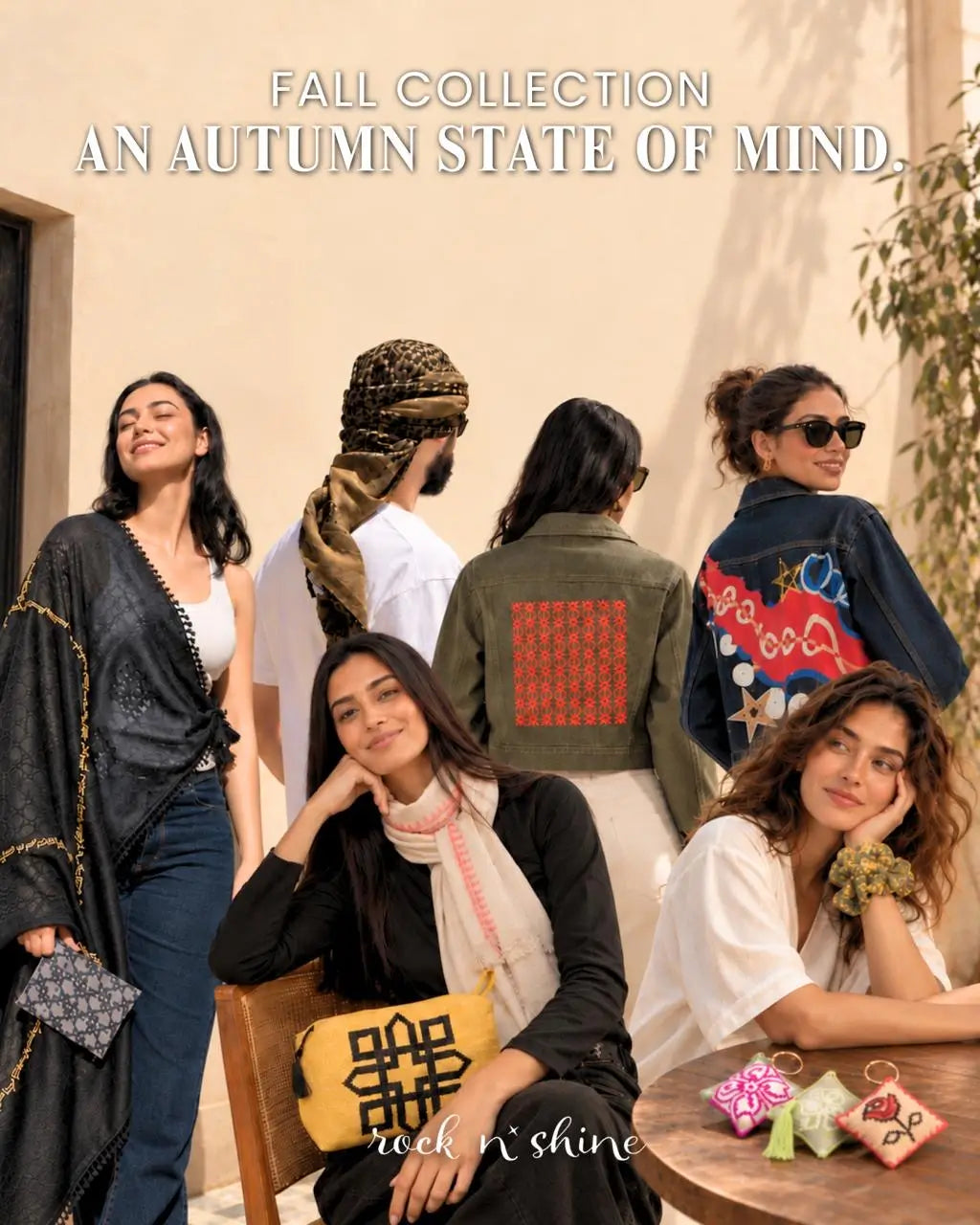 A fashion editorial group shot for the 'Autumn Collection' by 'rock n' shine', featuring multiple models showcasing various autumn outfits, including a black patterned shawl, an olive green jacket with a red geometric patch, a navy blue denim jacket with colorful embroidery, and a yellow patterned clutch bag.