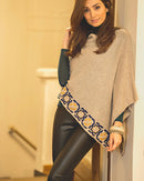 Woman wearing a beige poncho with a patterned edge in an indoor setting