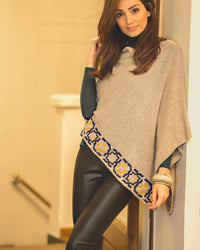 Woman wearing a beige poncho with a patterned edge in an indoor setting